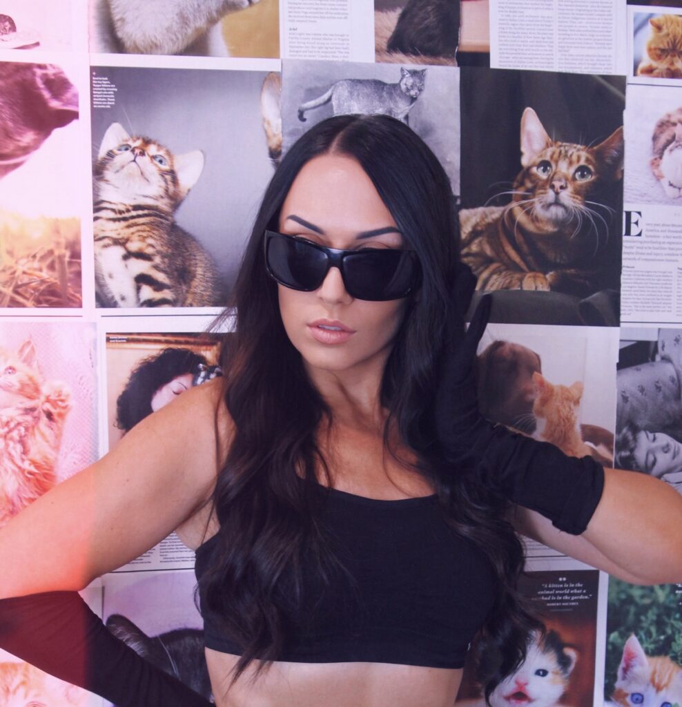 female dj with black sunglasses and clothing with cats in background